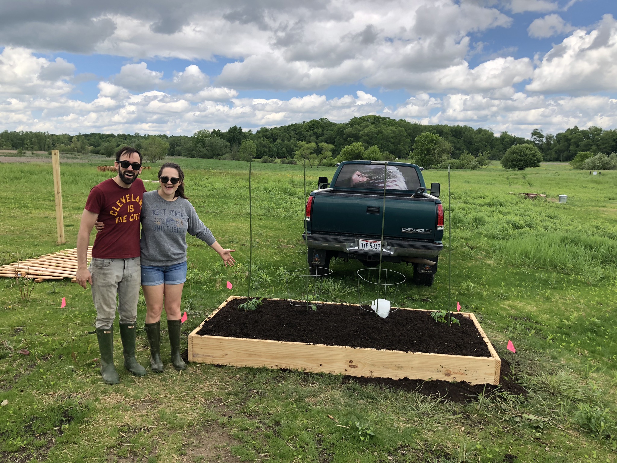 Keith and Emily Schmader standing proudly beside their first raised garden bed with the pickup truck and open pasture behind them